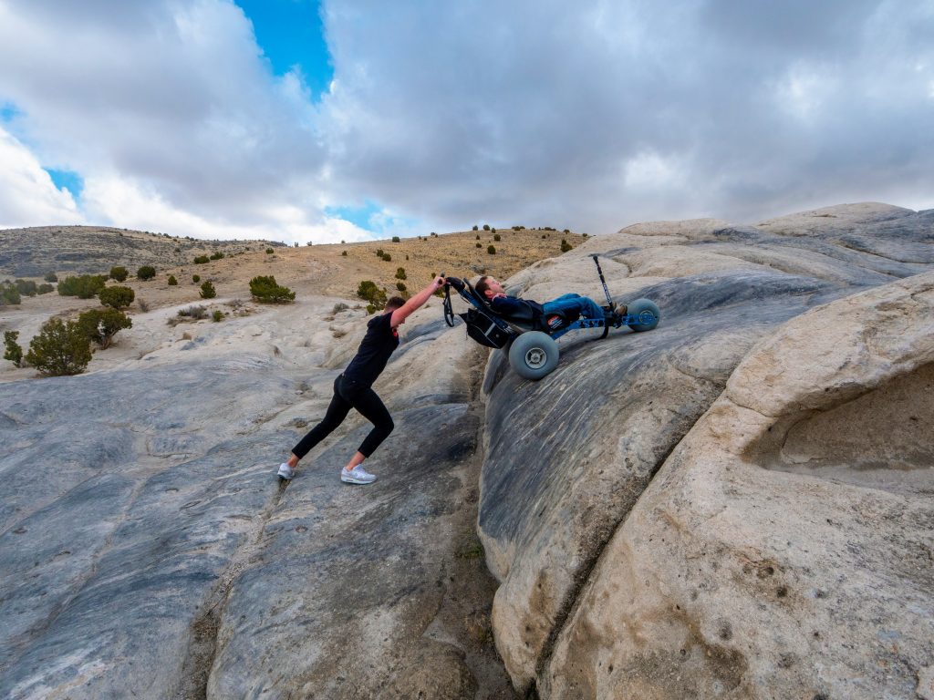 A man with cerebral palsy is pushed up a steep hill in an Extreme Motus All-Terrain Wheelchair.