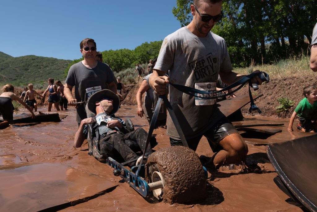 Man with cerebral palsy is helped by friends and his Extreme Motus off-road wheelchair to float across an water obstacle in the Dirty Dash obstacle course. 