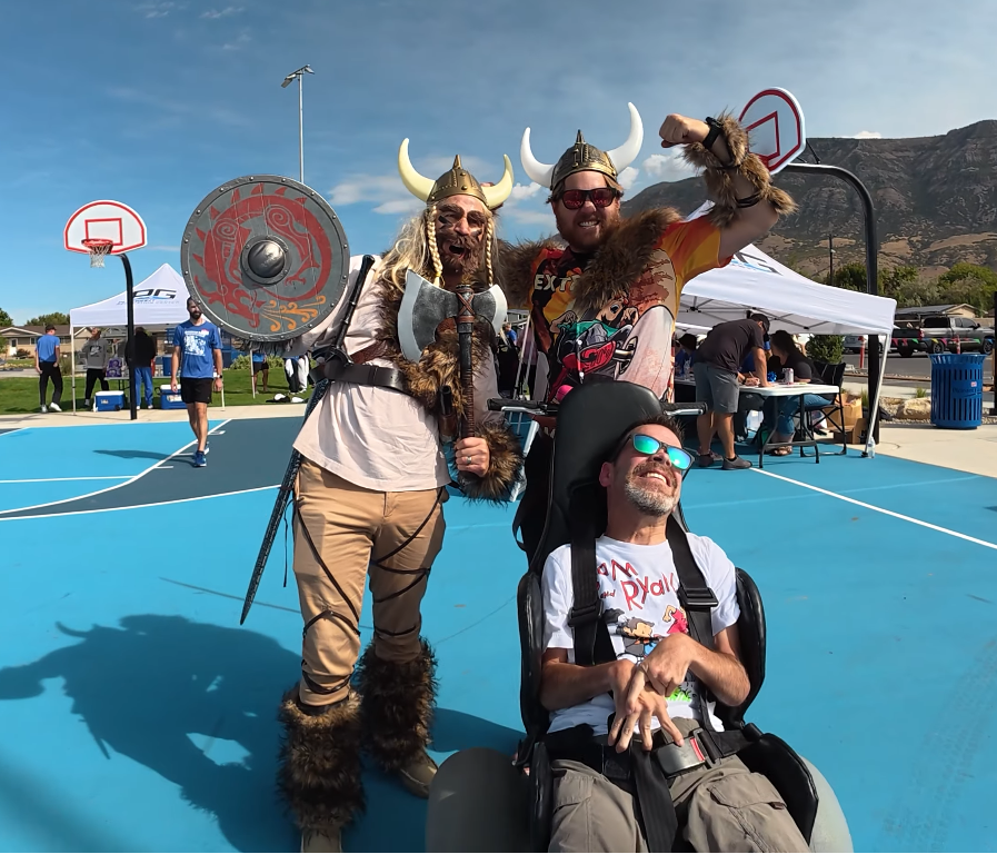 Two men dressed as Vikings pose next to a man in an all terrain wheelchair.