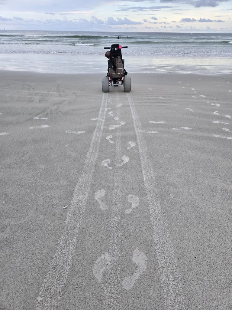 footprints in the sand lead to a beach wheelchair near the ocean.