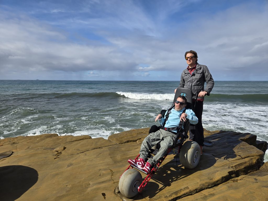 Sam & Ryan on a rocky beach with the extreme motus all terrain wheelchair. 