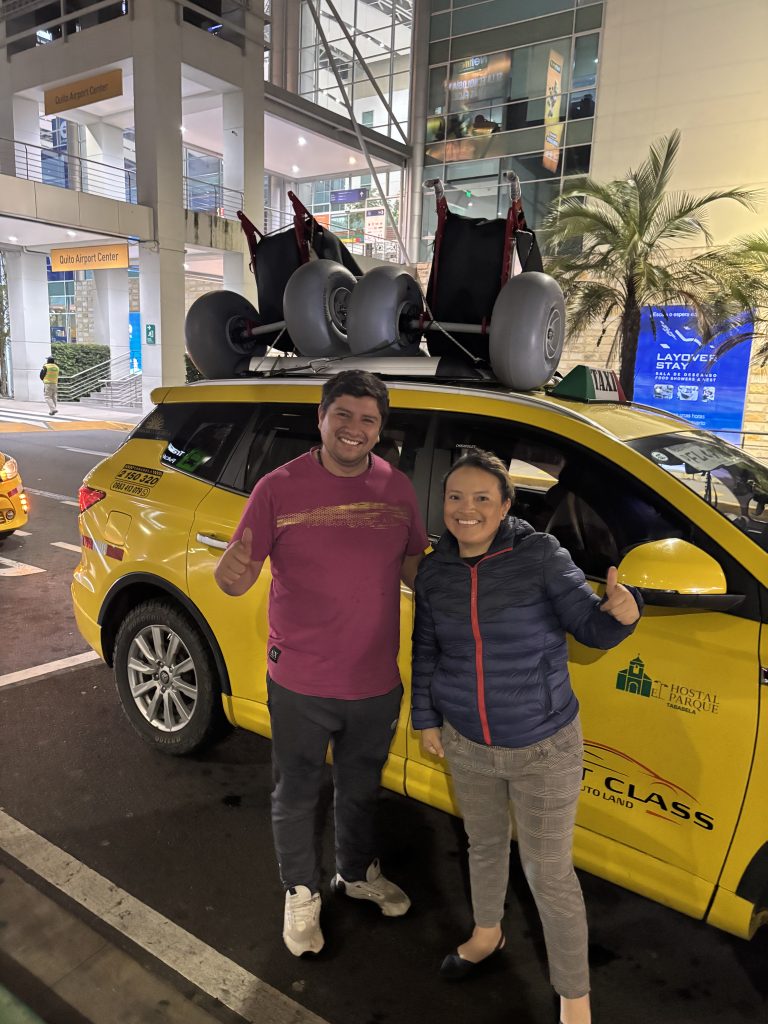 Two Extreme Motus all-terrain wheelchairs strapped to the roof of a yellow taxi outside Quito airport, Ecuador