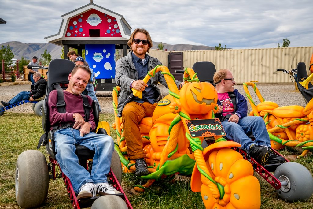 Three riders in Extreme Motus all-terrain wheelchairs on the giant pumpkin cars at Cornbelly's in Spanish Fork, Utah